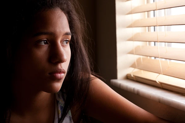Young person looking sad, looking out a windo